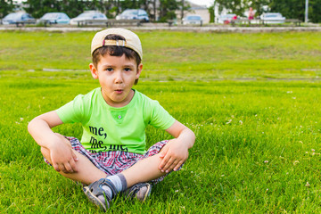 Wall Mural - happy boy sitting on the grass in the summer