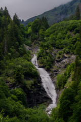 Fotomurales - vertical view of a high picturesque waterfall in lush green forest landscape