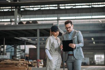 Manager talking with a female factory worker at large metal manufacturing plant.