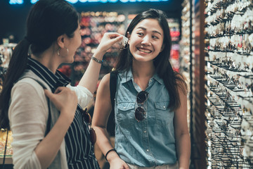 Wall Mural - two pretty young asian female friends trying pair of earrings while shopping at jewelry store together. girl helping smiling sister choose accessories in fashion shop. happy women spend leisure time