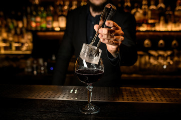 Bartender puts big ice cube in a cocktail