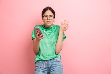 Sticker - Photo of displeased young girl wearing round eyeglasses using earphones while holding smartphone