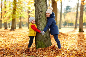 Poster - childhood, season and family concept - happy children at tree trunk in autumn park