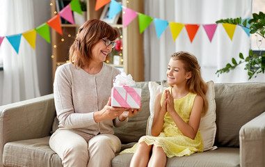 Canvas Print - family, greetings and celebration concept - happy grandmother giving her granddaughter birthday gift at home