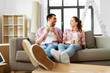 © Syda Productions - moving, people, repair and real estate concept - happy couple sitting on sofa and drinking coffee at new home