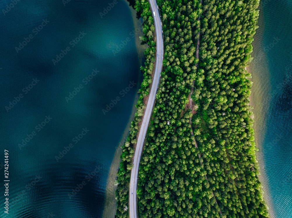 Aerial view of road between green forest and blue lake in Finland - obrazy, fototapety, plakaty 