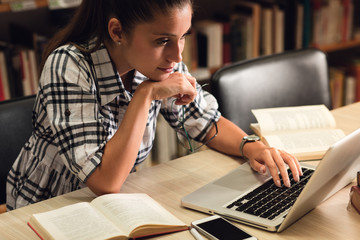 Wall Mural - Young female student study in the library using laptop for researching online.