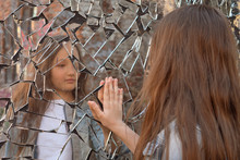 Young Girl Looks In A Broken Mirror And Shows Her Hand On A Mirror.