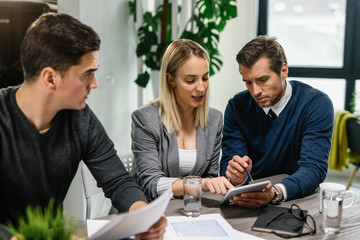 Insurance agent and young couple using digital tablet on a meeting at home.