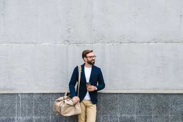 Wall Mural - Portrait of attractive businessman wearing eyeglasses holding paper cup and carrying bag