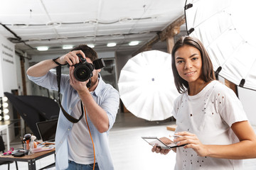 Poster - Portrait of young fashion team photo shooting model with professional camera and softbox in studio