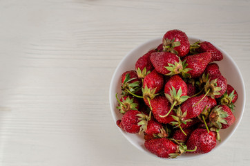 Fresh summer ripe strawberries in a white plate on a white wooden background