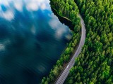 Aerial view of road between green forest and blue lake in Finland