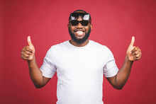 Funny Guy In White T-shirt And Sun Glases Jumping And Looking At Camera. Studio Portrait Of Emotional African Male Model Posing On Red Background. Thumbs Up.