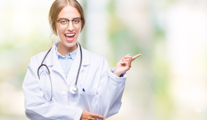 Canvas Print - Beautiful young blonde doctor woman wearing medical uniform over isolated background with a big smile on face, pointing with hand and finger to the side looking at the camera.