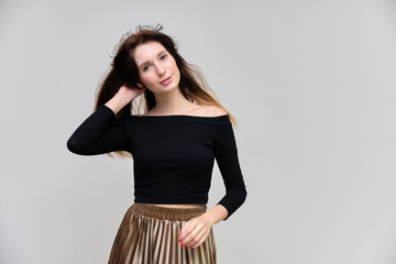 Photo portrait of a beautiful pretty brunette girl in a black sweater on a gray background. A woman is satisfied with her life, she stands in front of the camera, smiling and talking. Made in studio.