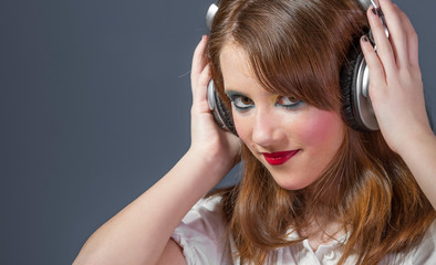 Wall Mural - Entertainment redhead girl with helmet on her head listening to music on a flat gray background