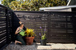 © Cavan Images - Woman watering potted plant while kneeling by fence at backyard