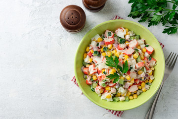 Wall Mural - Salad with crab sticks, sweet corn, cucumbers, boiled eggs, onion and rice in bowl on concrete background. Russian cuisine. Top view. Copy space.