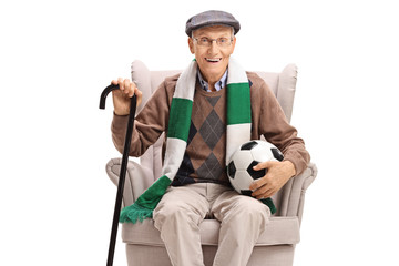 Canvas Print - Senior man with a football and a scarf sitting in an armchair