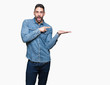 © Krakenimages.com - Young handsome man over isolated background amazed and smiling to the camera while presenting with hand and pointing with finger.