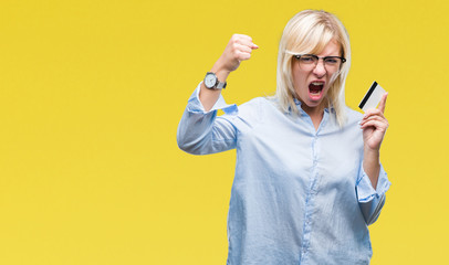 Poster - Young beautiful blonde business woman holding credit card over isolated background annoyed and frustrated shouting with anger, crazy and yelling with raised hand, anger concept