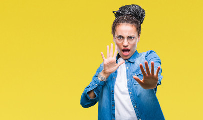 Poster - Young braided hair african american girl wearing glasses over isolated background afraid and terrified with fear expression stop gesture with hands, shouting in shock. Panic concept.