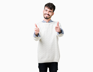 Young handsome man wearing winter sweater over isolated background approving doing positive gesture with hand, thumbs up smiling and happy for success. Looking at the camera, winner gesture.