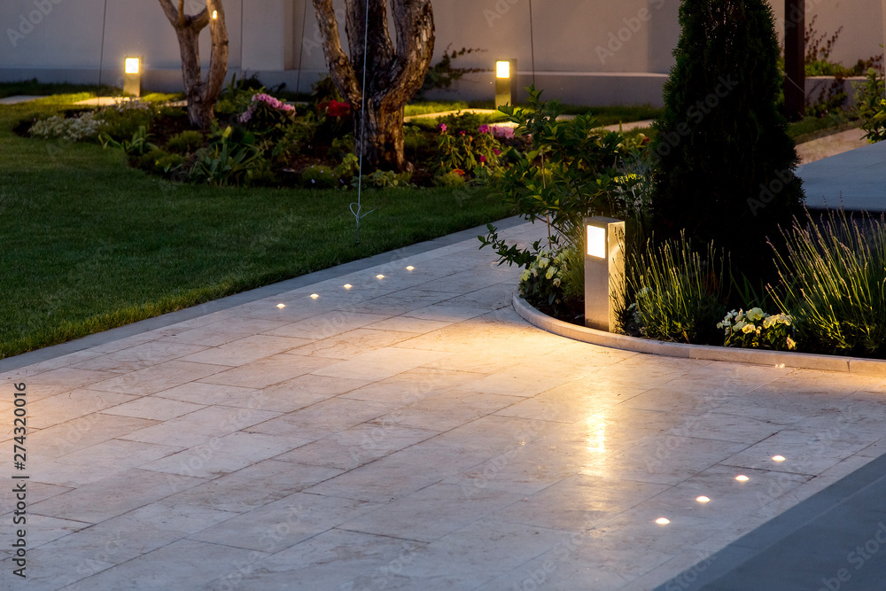 marble tile playground in the backyard of flowerbeds and lawn with ground lantern and lighting in the warm light at dusk in the evening. - obrazy, fototapety, plakaty 