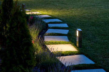 marble path of square tiles illuminated by a lantern glowing with a warm light in a backyard garden 