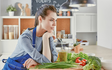 Happy young woman in kitchen with fresh vegetables on the table