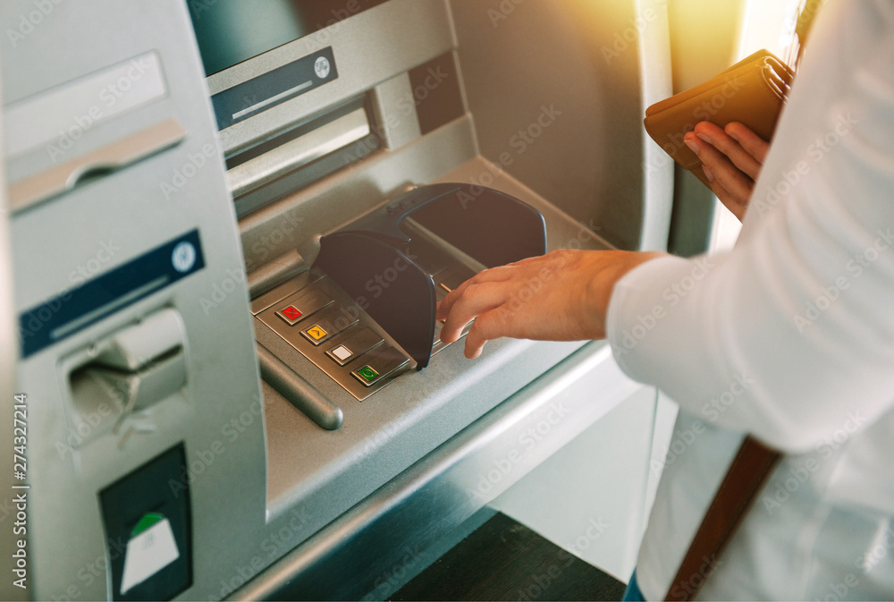 Woman using ATM holding wallet an pressing the PIN security number on the keyboard automatic teller machine - obrazy, fototapety, plakaty 