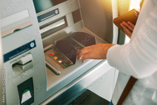 Woman using ATM holding wallet an pressing the PIN security number on the keyboa Poster Mural XXL