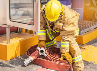 Fireman in yellow fire fighter uniform with rolled fire hose during prepare connect firehose tube in to fire hydrant