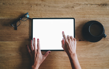 A woman's hands using an ipad on a wooden table with glasses and a cup of coffee