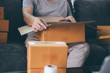 © wutzkoh - Asian entrepreneur teenager is opening a cardboard box in order to put the product that the customer ordered into the box to deliver the product.