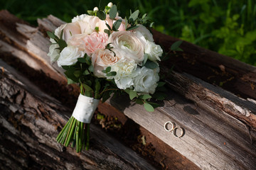 Details of the morning of the wedding day.a delicate wedding bouquet of white and pink roses outdoosand pions. a bridal bouquet and two gold wedding rings on a wooden background.