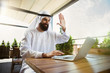 © master1305 - Arab saudi businessman working online with a laptop and tablet in a coffee shop or a cafe with an outdoor terrace in the background. Concept of business, finance, modern technologies, start up.
