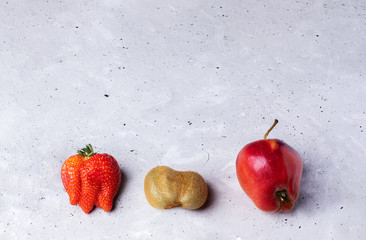 Wall Mural - Three ugly fruits: strawberry, kiwi and apple on grey concrete background. 