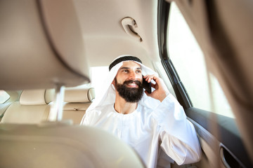 Arab saudi businessman working online with a smartphone, calling his clients or partners in his car. Male model as an enterpreneur. Concept of business, finance, modern technologies, start up, economy