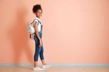 Stylish African-American girl in jeans overall near color wall