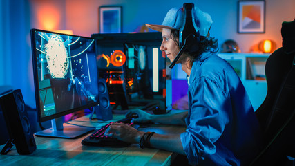 Wall Mural - Professional Gamer Playing First-Person Shooter Online Video Game on His Powerful Personal Computer. Room and PC have Colorful Neon Led Lights. Young Man is Wearing a Cap. Cozy Evening at Home.