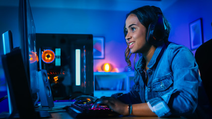 Wall Mural - Pretty and Excited Black Gamer Girl in Headphones is Playing First-Person Shooter Online Video Game on Her Computer. Room and PC have Colorful Neon Led Lights. Cozy Evening at Home.