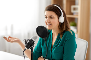 Wall Mural - technology, mass media and people concept - woman with microphone and headphones talking and recording podcast at studio