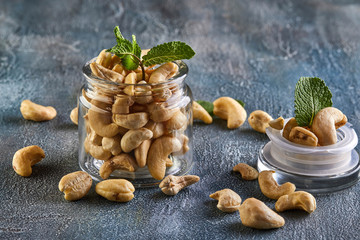 Poster - Cashew in a transparent jar with sheets of mint on top on a background with a blue tint.