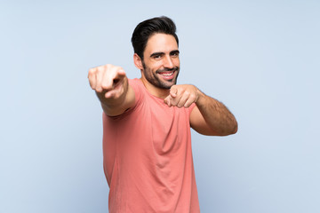 Handsome young man in pink shirt over isolated blue background points finger at you while smiling