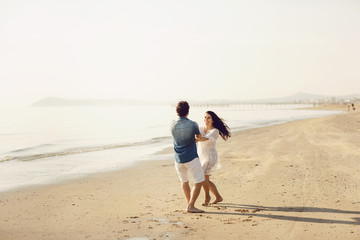 Happy couple in love has fun on the beach. They jump, laugh and enjoy the sea