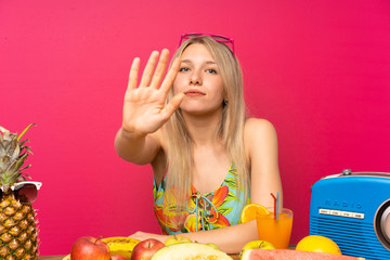 Poster - Young blonde woman with lots of fruits making stop gesture with her hand