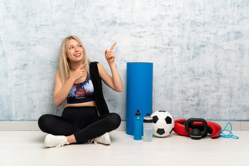 Young blonde sport woman sitting on the floor pointing with the index finger a great idea