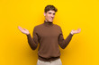 © luismolinero - Handsome young man over isolated yellow background holding copyspace with two hands